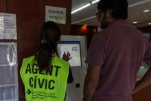 una persona que realitza treballs en benefici de la comunitat ensenya a un usuari el funcionament del caixer TESEO